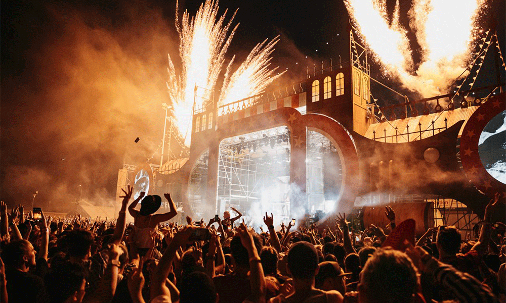 Outdoor festival at night time with fireworks exploding from the stage and the crowd jumping